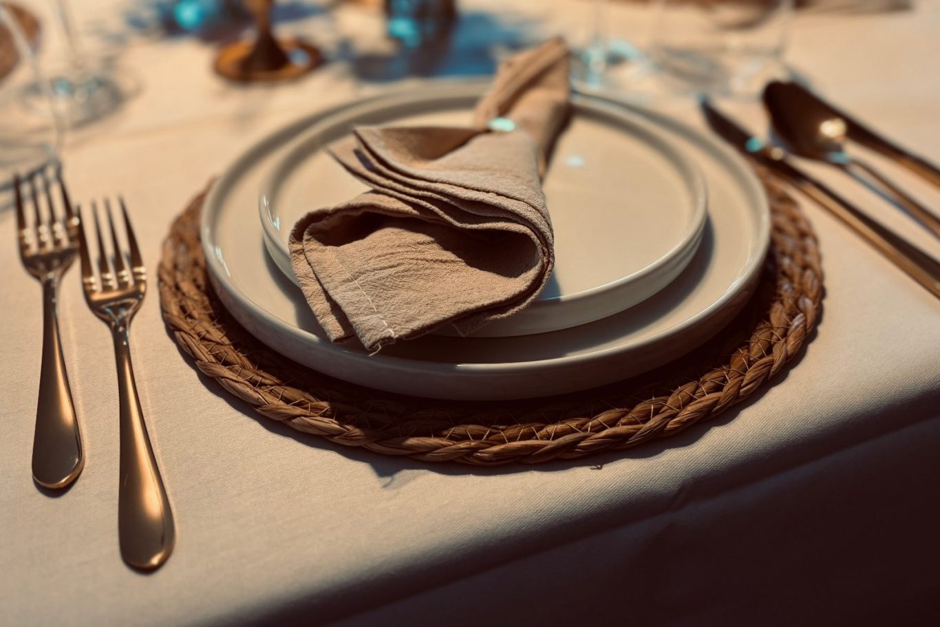 Tischgedeck mit Tellern, Besteck und gefalteter Serviette auf einem eleganten Tisch.