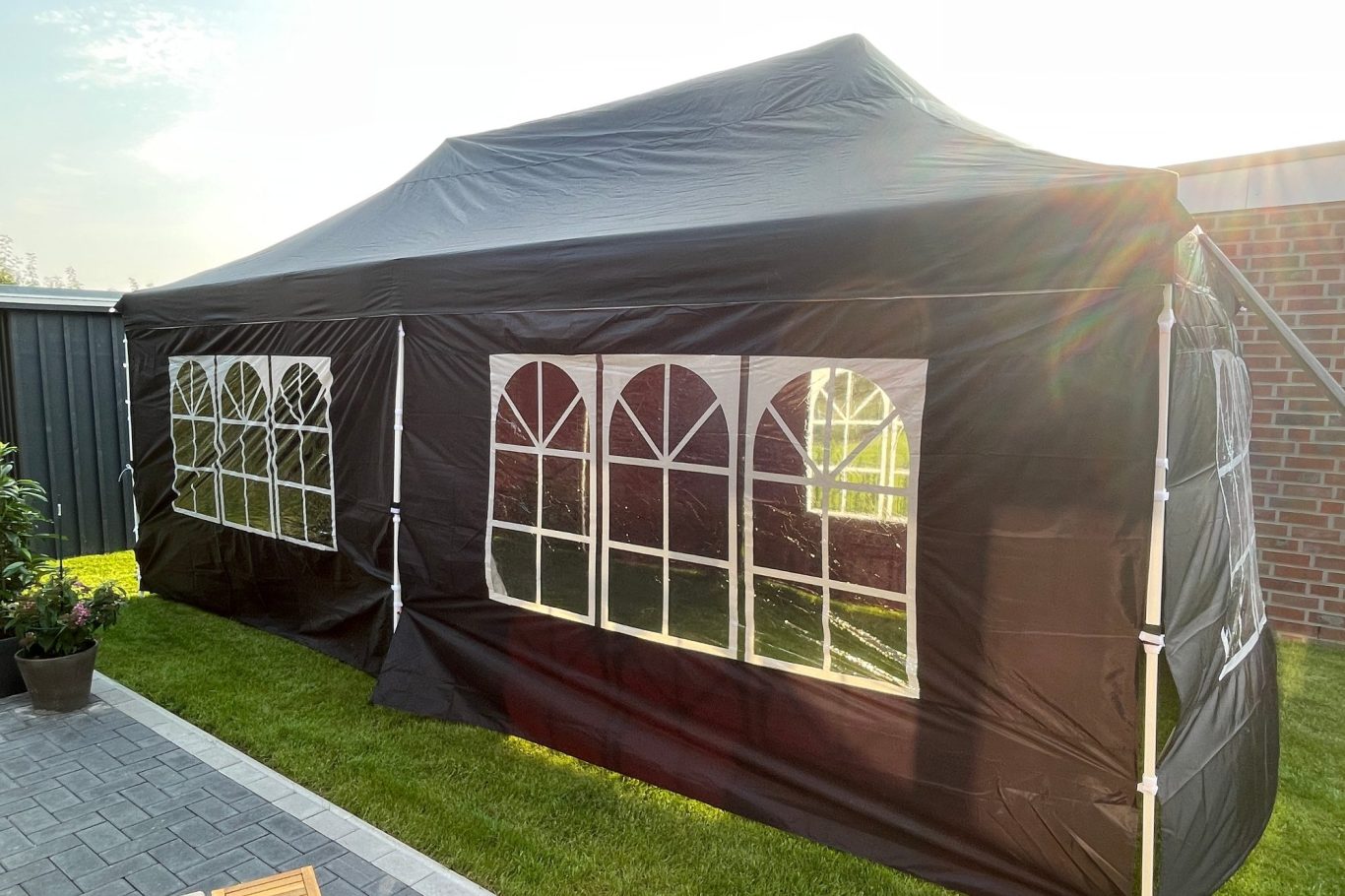 Schwarzes Partyzelt mit großen Fenstern im Garten unter Sonnenschein.