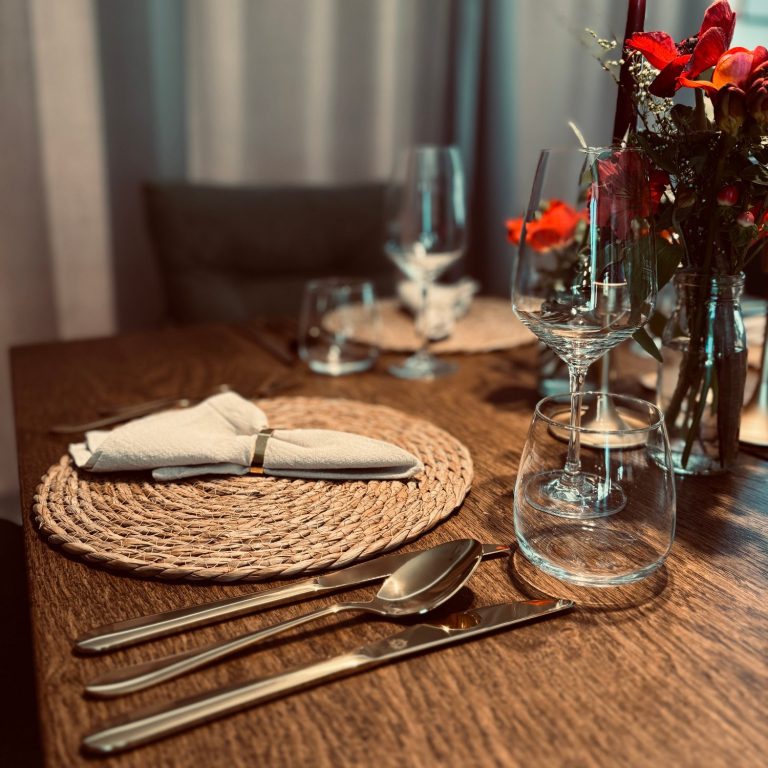 Elegant gedeckter Tisch mit Besteck, Gläsern und frischen Blumen.