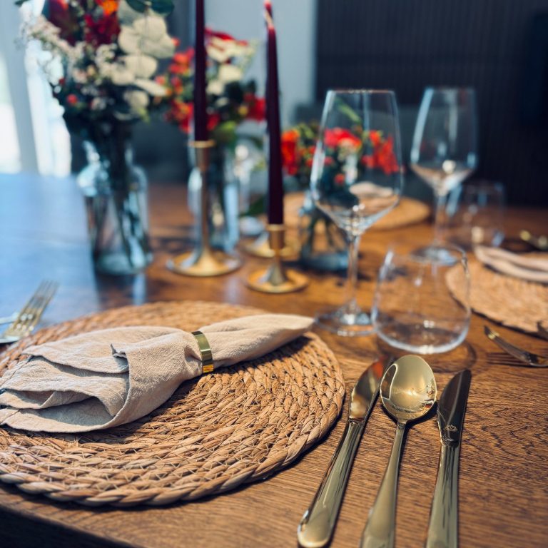 Elegant gedeckter Tisch mit Blumen, Kerzen, Gläsern und Silberbesteck.