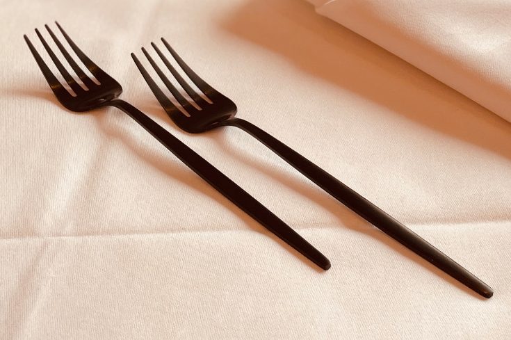 Zwei schwarze Gabeln liegen auf einer weißen Tischdecke.