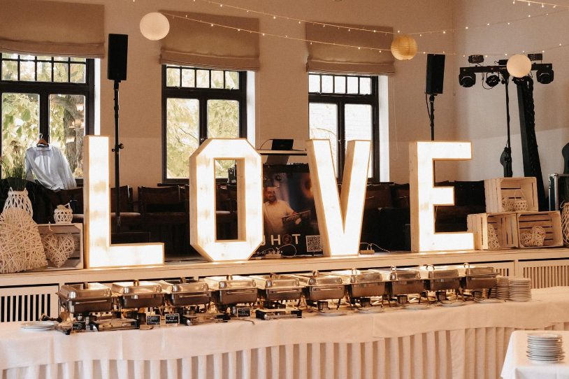 Beleuchtete Buchstaben "LOVE" vor einem eleganten Veranstaltungsraum.