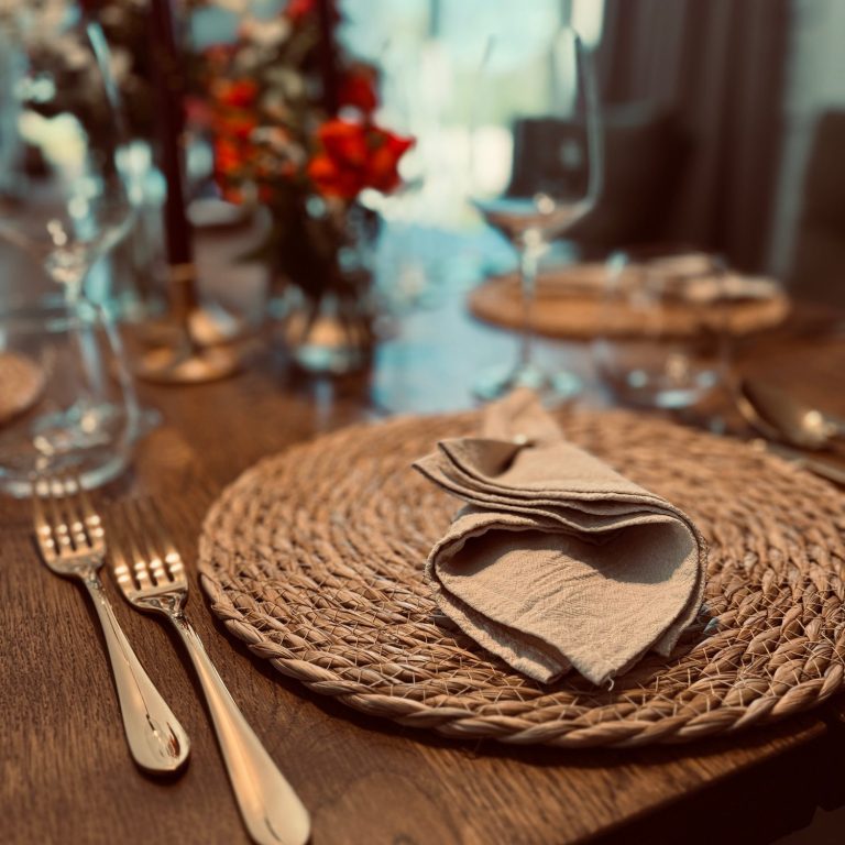 Ein gedeckter Tisch mit einer runden Platzmatte, Besteck und Servietten.